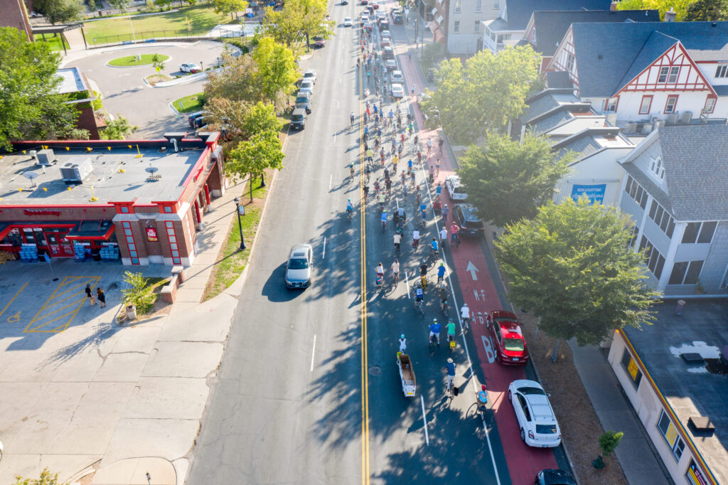 A hundred people on bikes on Hennepin Avenue. Bus lane filled with parked cars.